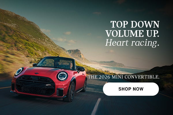 Red MINI convertible driving along a coastal road with mountains and ocean in the background