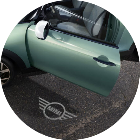 A parked MINI Cooper S 2 Door with the driver’s door open to reveal the MINI logo projection on the concrete beneath it.