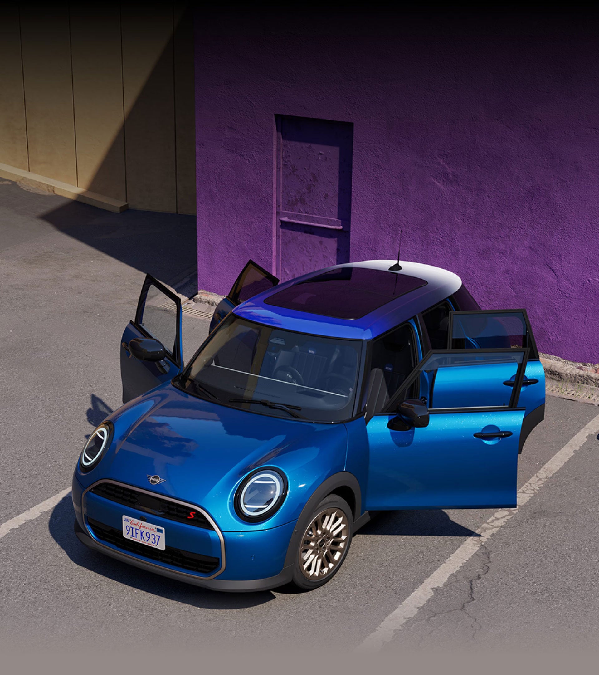 Birds-eye view of the MINI Cooper S 4 Door in Icy Sunshine Blue parked on a concrete surface with all four doors open and a purple concrete wall in the background.
